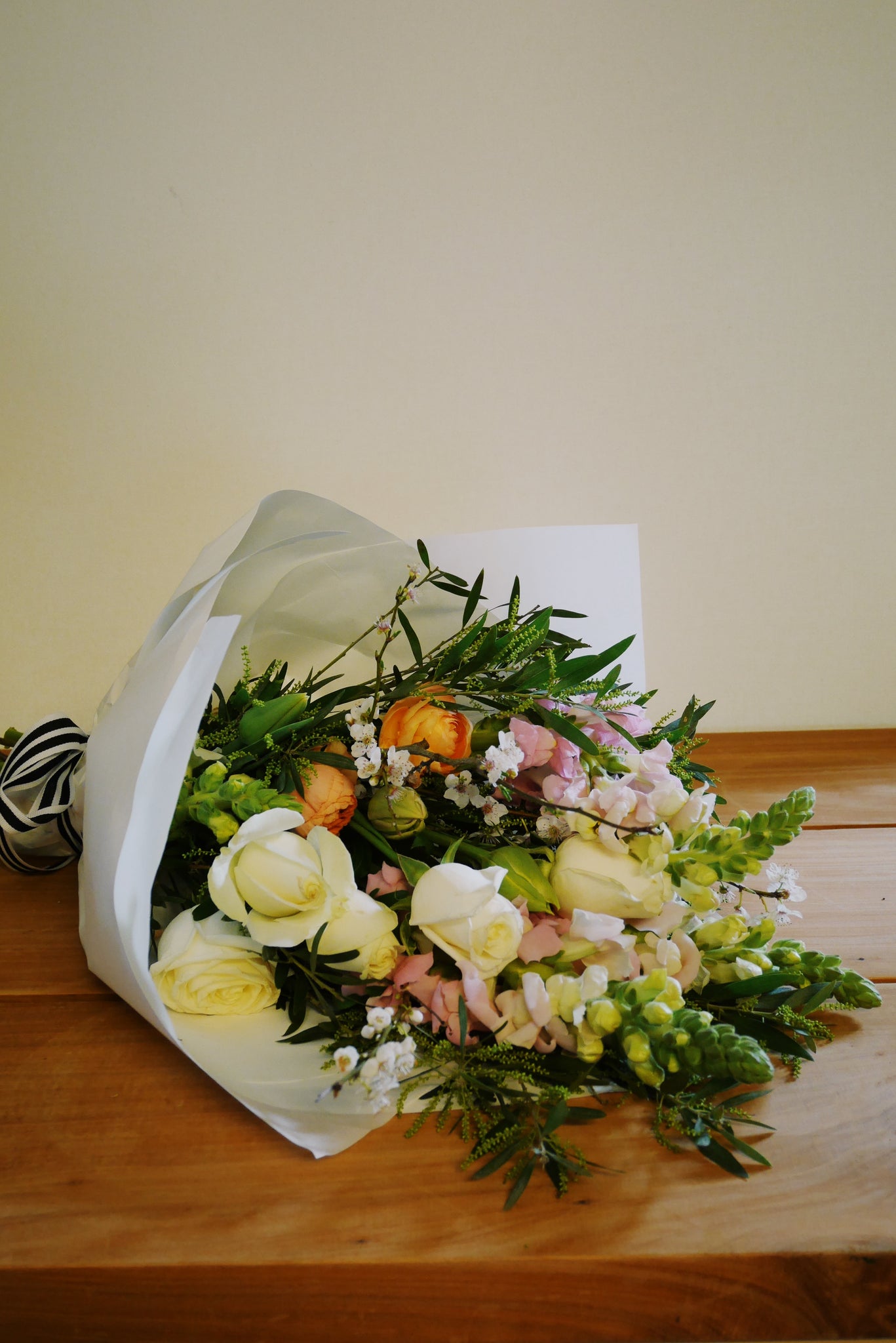 Bouquet of fresh flowers wrapped in white paper on a wooden surface with a plain background wrapped ready for local delivery