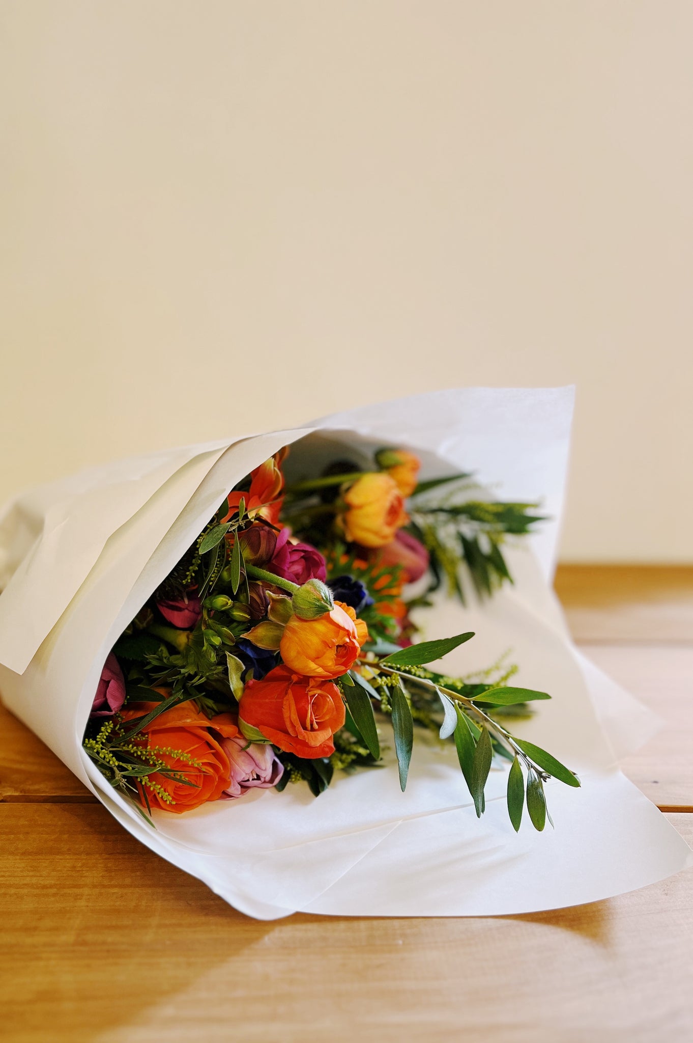 Bouquet of fresh flowers wrapped in white paper on a wooden surface with a neutral background